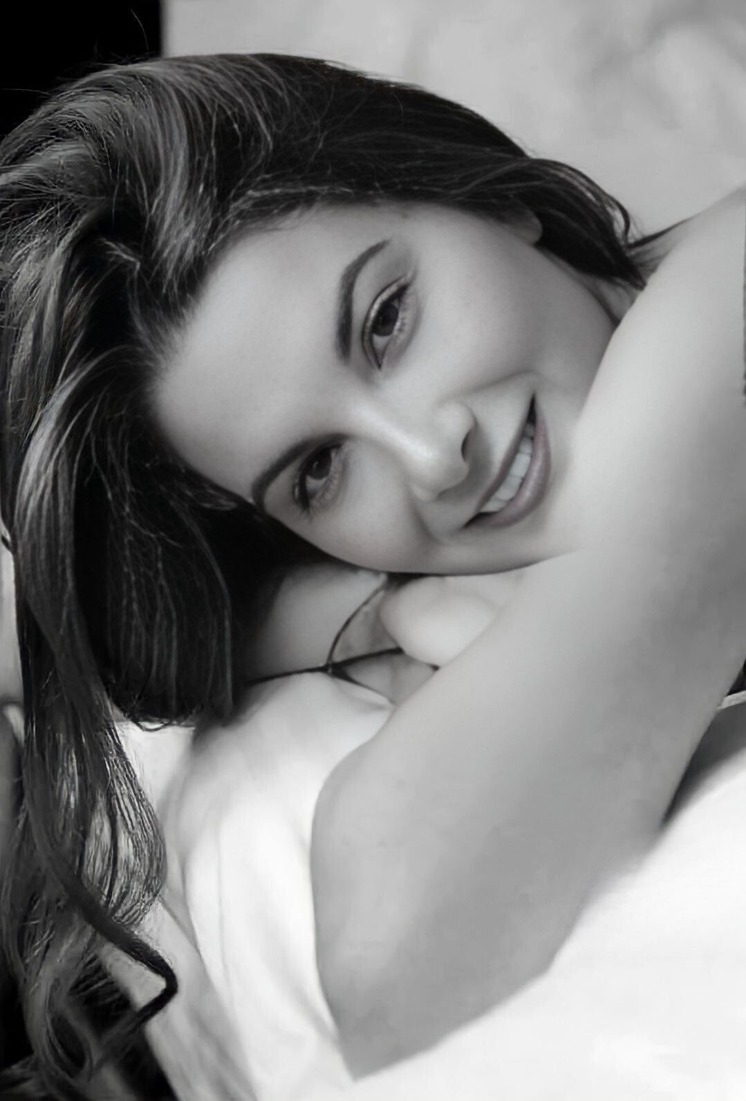 Susurro — retrato íntimo en blanco y negro de una mujer recostada con sonrisa suave y luz delicada